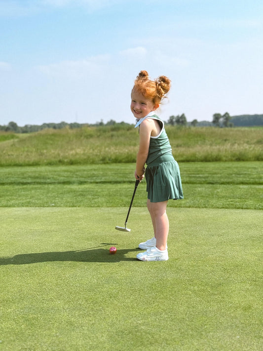 Toddler girl ages 2-5 playing kids golf outdoors with putter on green grass field