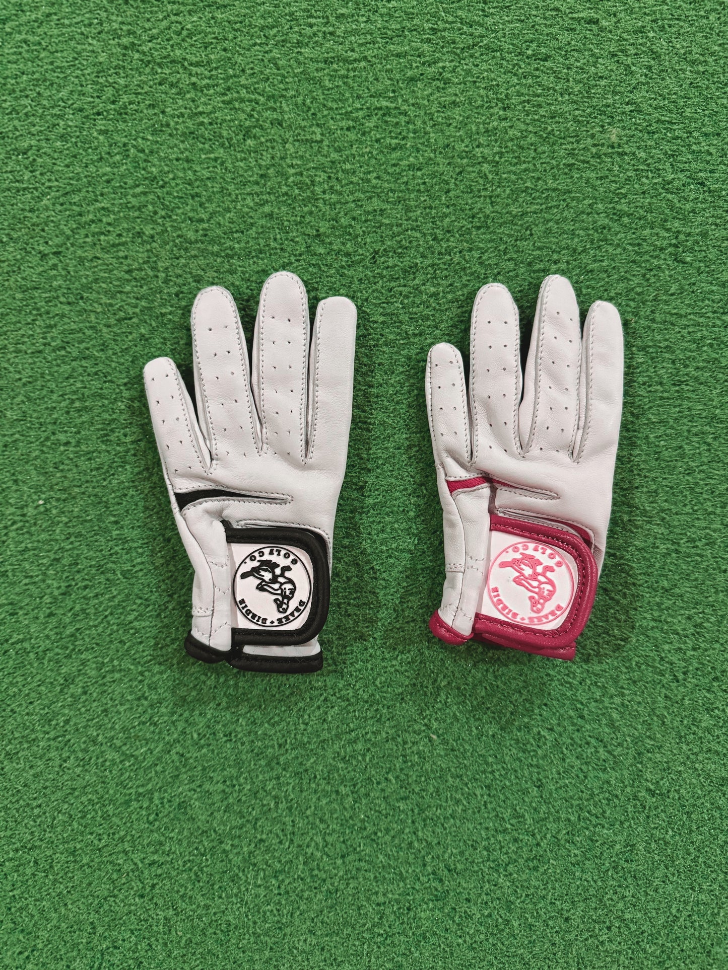 Two white golf gloves with brand logos on a green surface