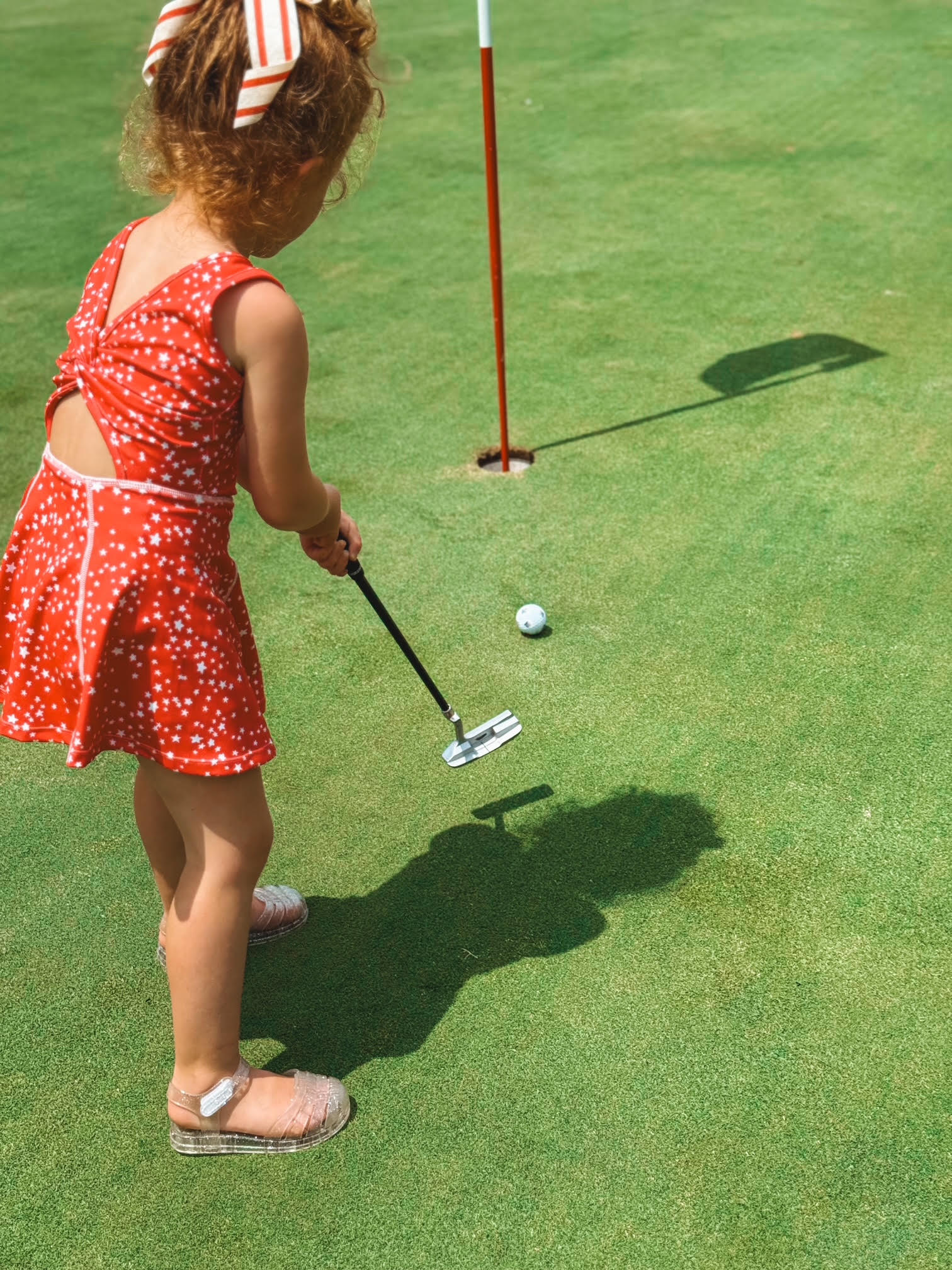 Child in a red dress playing golf on a green course