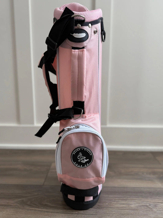 Pink golf bag with black straps on a wooden floor.